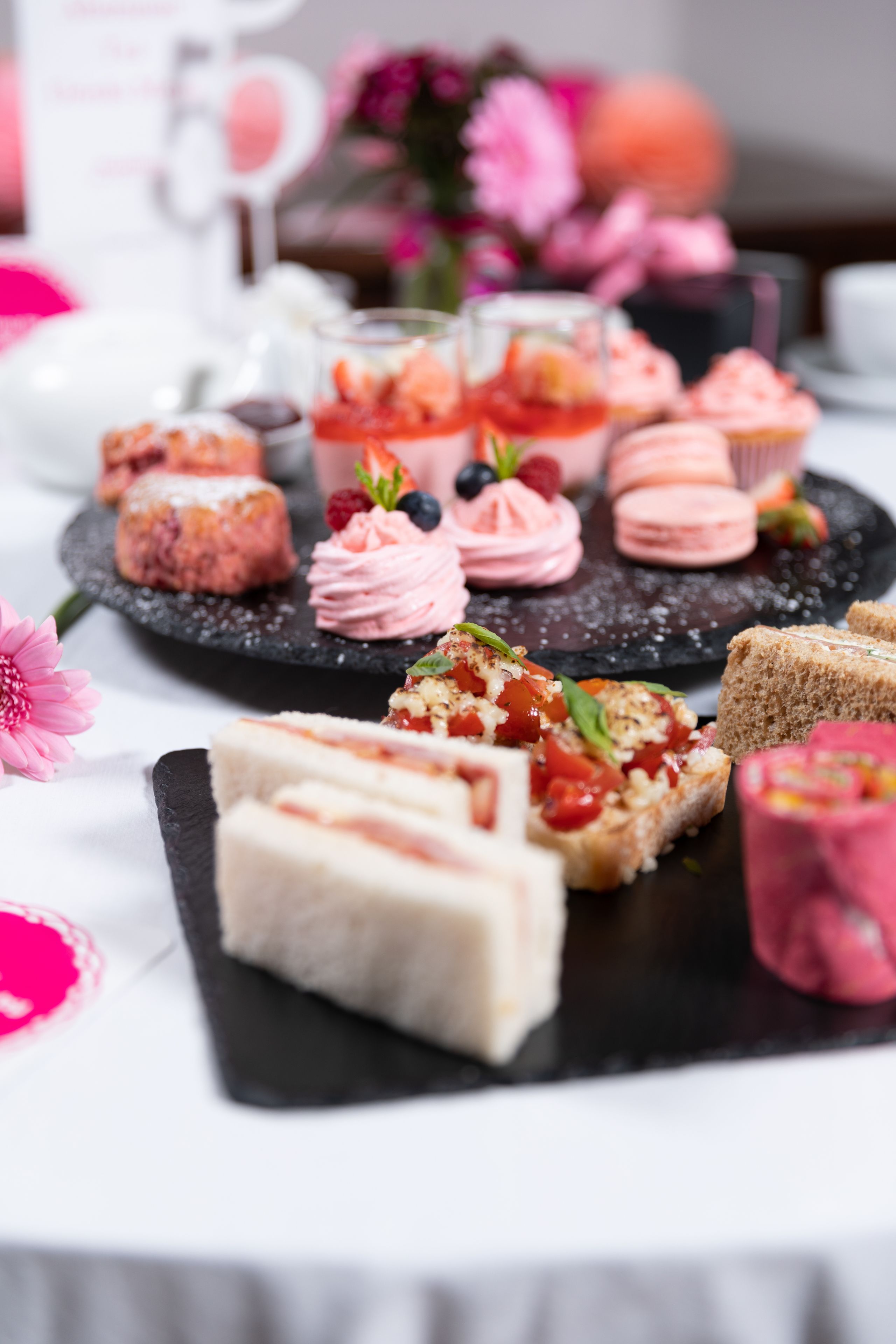 Diversos doces em um suporte de ardósia, incluindo macarons, pastéis e bolos com fruta.