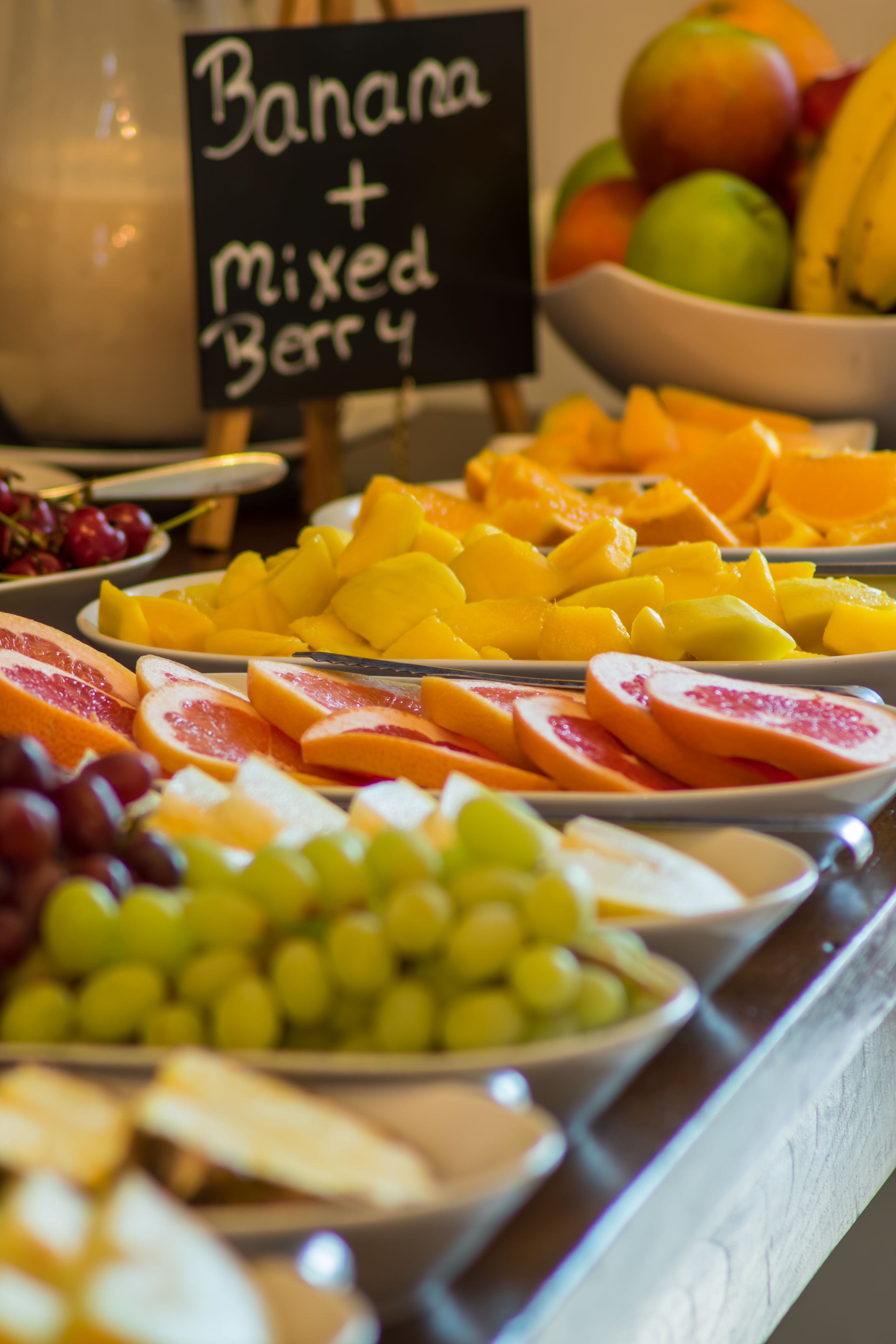 Un présentoir de fruits avec différents types de fruits et une pancarte indiquant « Banane + mélange de baies ».