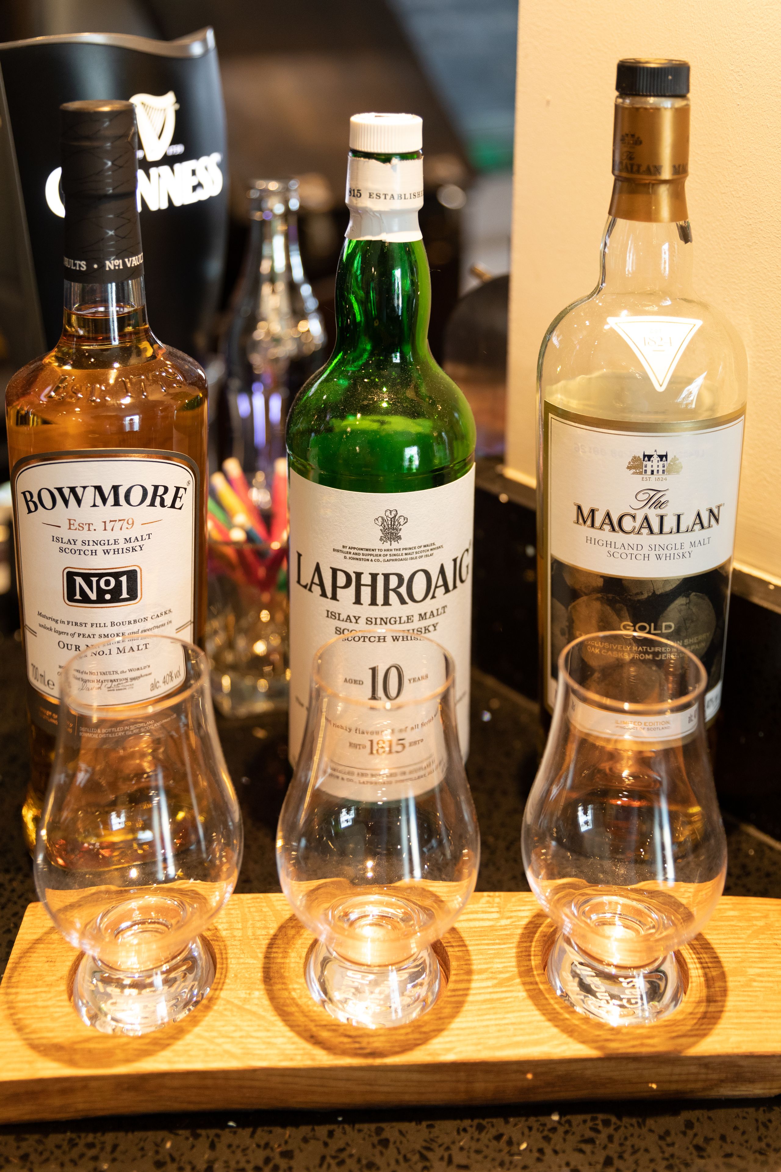 Tres botellas de whisky y dos vasos vacíos sobre una bandeja de madera.