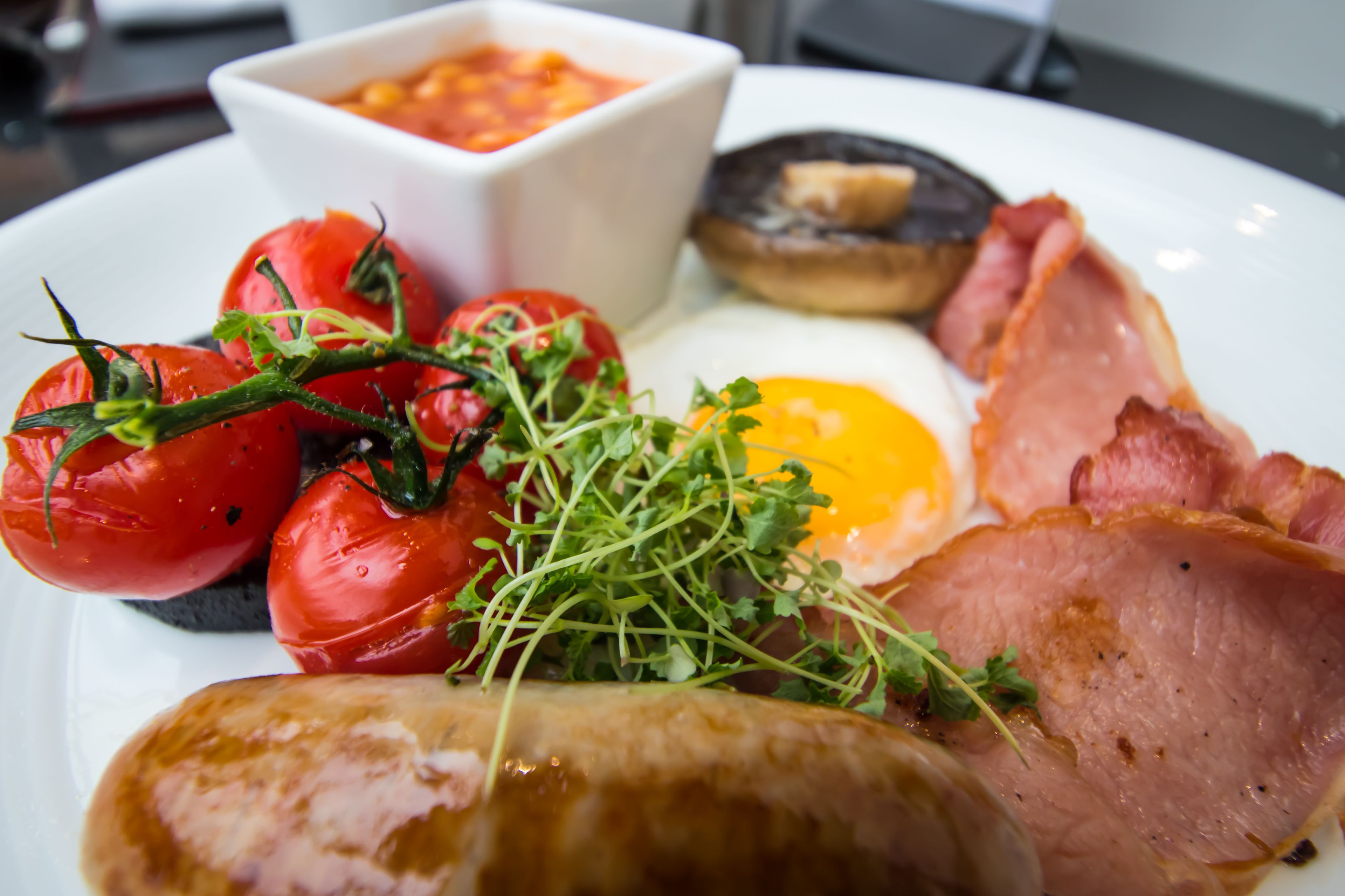 A plate with a variety of foods including tomatoes, greens, a fried egg, ham, and sausages.