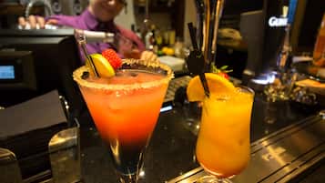 Zwei Cocktails auf einer Bar, ein Barkeeper ist im Hintergrund zu sehen.