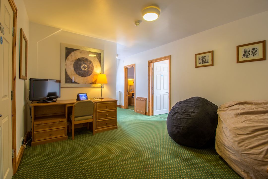 A hotel room with a bed, a desk with a computer, a television, and a large bean bag.