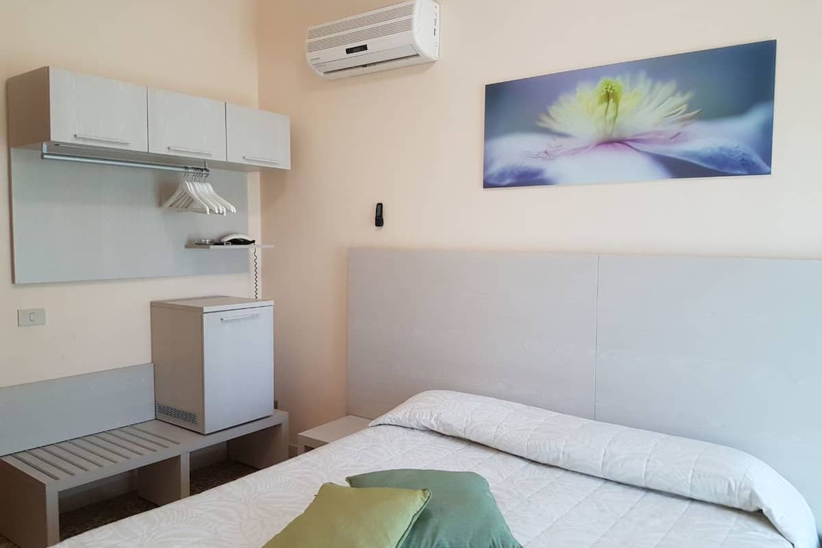 Een hotelkamer met een bed, een bureau, een kledingkast, een airconditioner en een bloemschilderij aan de muur.