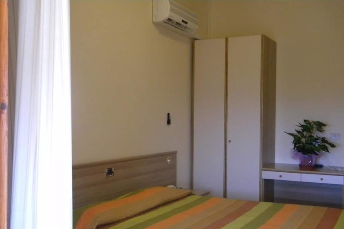 Een slaapkamer met een bed, een kledingkast, een bureau en een kamerplant.