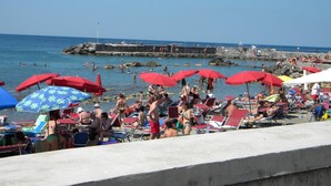 Una playa concurrida con sombrillas rojas y gente nadando.