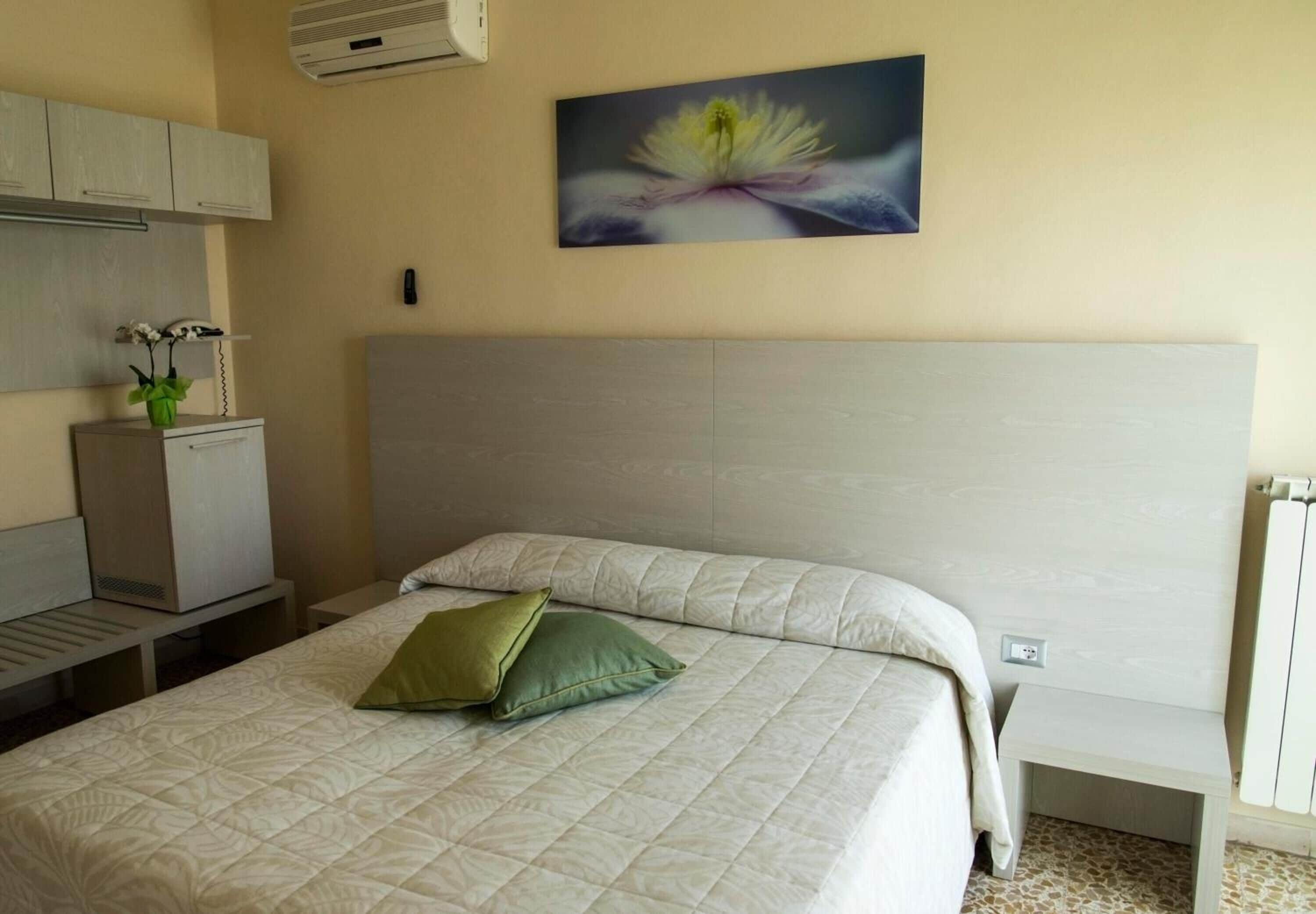 Quarto de hotel com cama, escrivaninha, cadeira, radiador e ar condicionado fixado na parede.