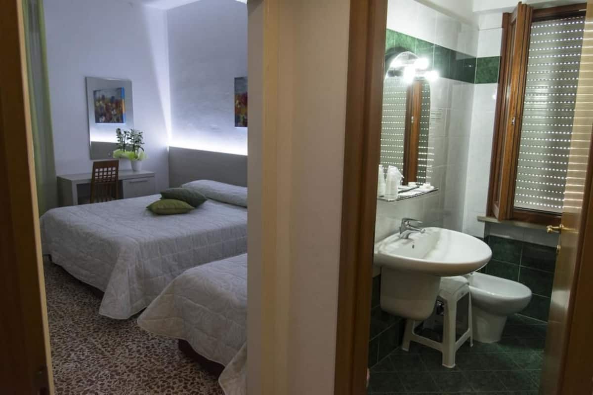 Een slaapkamer met twee bedden, een nachtkastje met een lamp en een klein bureau met een stoel.