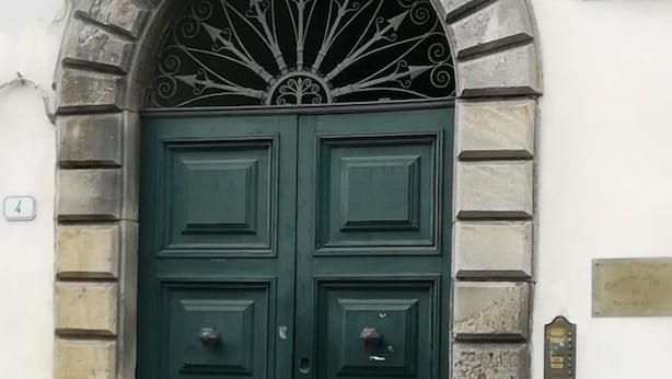 A green double door with a decorative metal arch above it, set in a stone wall. - Corte dei Nobili (Lucca)
