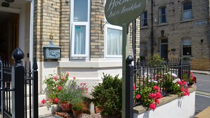 Señal para 'Hollea Bed & Breakfast', un edificio de ladrillo y una valla de hierro negro adornada con flores.