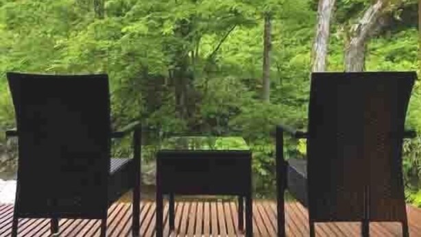 An outdoor seating area with two chairs and a table, surrounded by a wooden deck and dense green foliage. - Yamado (Nishiwaga)