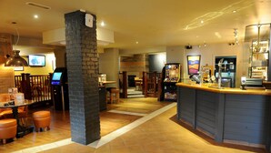 A bar area with a counter, stools, and a television screen. - Premier Inn York North West (York)