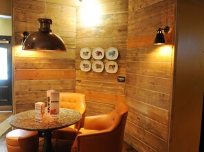 A corner room with wooden walls, a round table with a drink menu, a single orange chair, and wall-mounted plates with animal designs. - Premier Inn York North West (York)