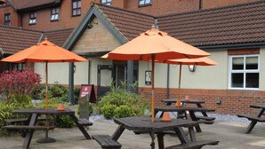 Outdoor picnic tables with orange umbrellas, a brick building with a sign reading 'The Millfield,' and a signboard for Costa Coffee. - Premier Inn York North West (York)