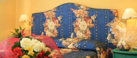 Een slaapkamer met een bloemenbekleed hoofdbord, twee bedlampen, een nachtkastje in groen en een rozenboeket.