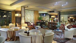 Eine Hotelhalle mit weißen Sesseln, einem Glastisch, einem Klavier und einem Fernseher.