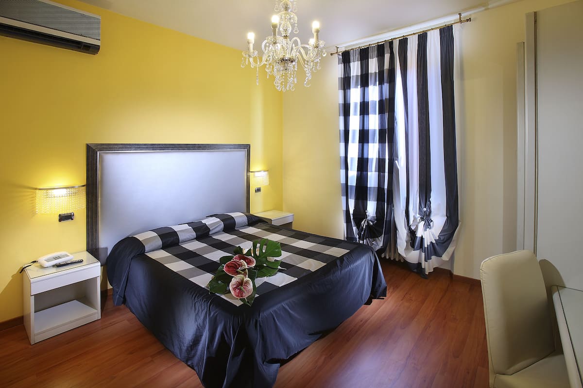Ein Schlafzimmer mit einem großen Bett, Nachttischlampen, einem Nachttisch mit Telefon, einer Kristallleuchtreiter und einer karierten Bettdecke.