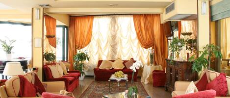 A spacious living room with red and beige furniture, a glass coffee table, and a large window with curtains.