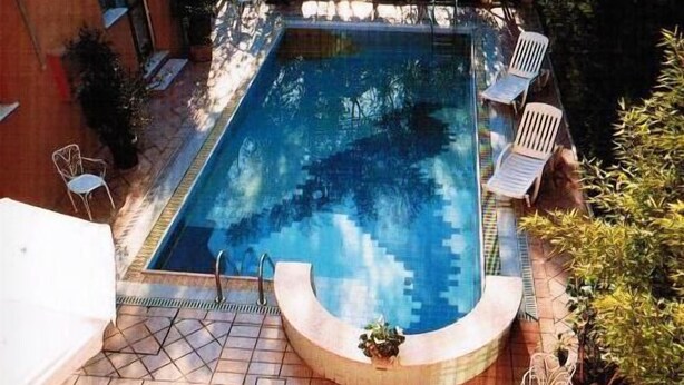 Ein rechteckiger Pool mit gewölbter Kante, umgeben von einer gefliesten Terrasse.