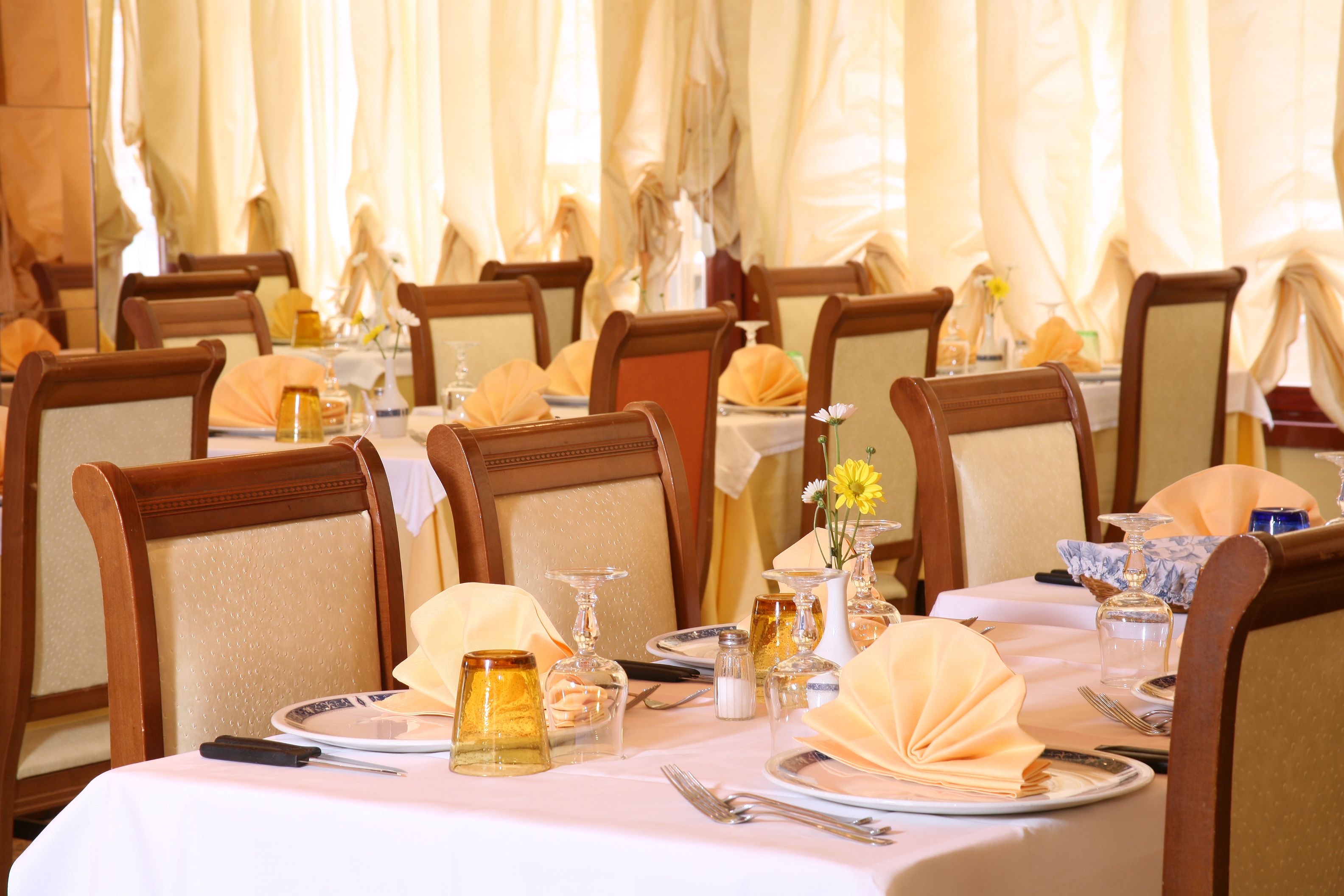A dining area with tables set for a meal, chairs, and a vase with flowers.