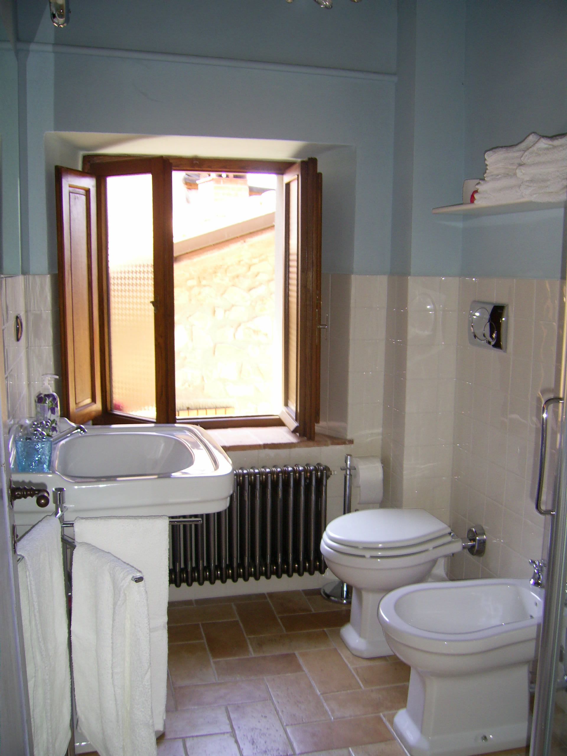 A bathroom with a sink, toilet, bidet, and a window.