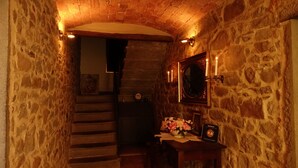 A narrow stone-walled hallway with a wooden staircase, a small table with a vase of flowers, and a framed picture on the wall. - Casa Vacanze Le Muse Sillico (Pieve Fosciana)