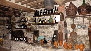A rustic cellar with stone walls, wooden beams, and shelves filled with wine bottles and pottery. - Casa Vacanze Le Muse Sillico (Pieve Fosciana)