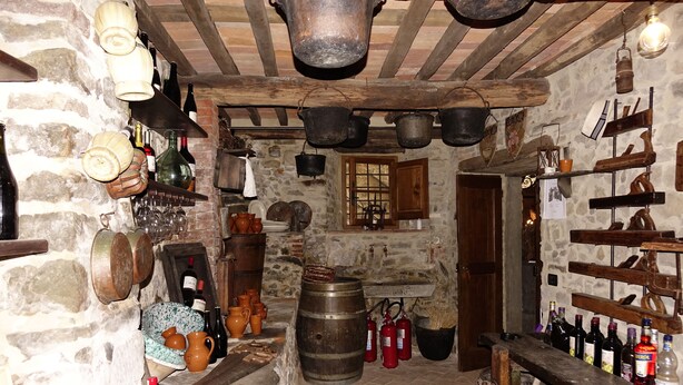 A rustic kitchen with stone walls, wooden beams, and various kitchen utensils and bottles. - Casa Vacanze Le Muse Sillico (Pieve Fosciana)