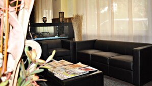Un salon moderne avec un canapé noir, une table basse sur laquelle sont posés des magazines, un aquarium et un vase contenant des plantes séchées.