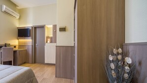 Une chambre d’hôtel équipée d’un lit, d’un bureau, d’une télévision, d’un radiateur et d’une plante décorative.