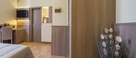 Una habitación de hotel con cama, escritorio, televisor, radiador y una planta decorativa.