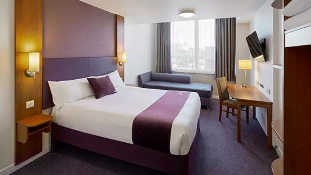 A hotel room with a large bed, a desk, a chair, a sofa, and a TV.
