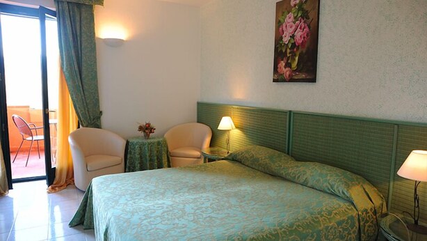 Ein Hotelzimmer mit Bett, zwei Stühlen, einem kleinen Tisch mit Blumenvase und einem Bild an der Wand.