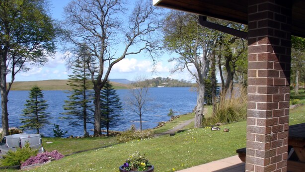 Blick auf einen See mit einer Terrasse, einer Ziegelstütze und einem Blumentopf.