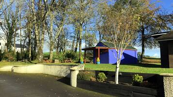 A small, colorful playhouse labeled "Games Room" surrounded by trees and a grassy area.