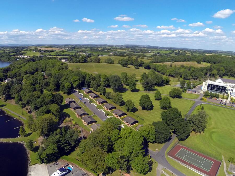 An aerial view of a residential area with a large house, a tennis court, and a lake.