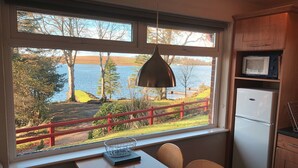 Eine Küche mit einem großen Fenster mit Blick auf einen See, einem roten Geländer und einem Essbereich mit Stühlen und einem Tisch.