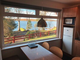 Una cocina con un ventanal grande que da a un lago, barandilla roja y comedor con sillas y mesa.
