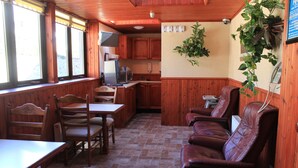 Interior acogedor de una cabaña con paredes de madera, un comedor con mesa y sillas, una cocina con microondas y un espacio de estar con sillones de cuero.