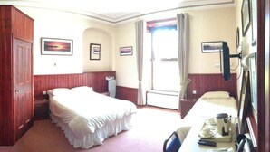 Habitación de hotel con cama, escritorio con silla, armario y ventana con cortinas.