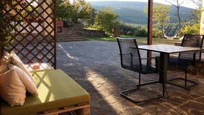 An outdoor patio with stone flooring, a wooden bench, and a table with chairs. - Podere Bellavista (San Gimignano)