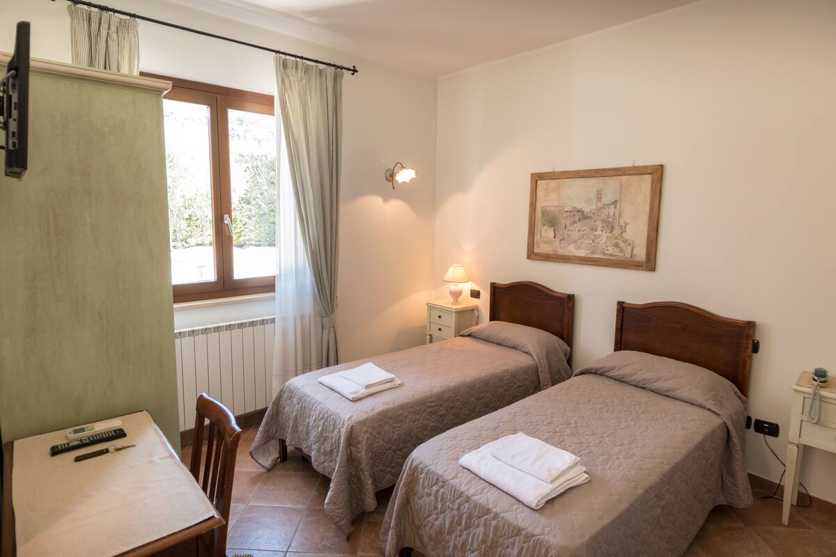 A room with two beds, a desk, a chair, a lamp, and a painting on the wall.
