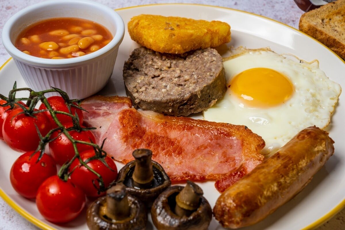 Une assiette de nourriture pour le petit-déjeuner comprenant des œufs, des saucisses, du bacon, des champignons, des tomates et des haricots.