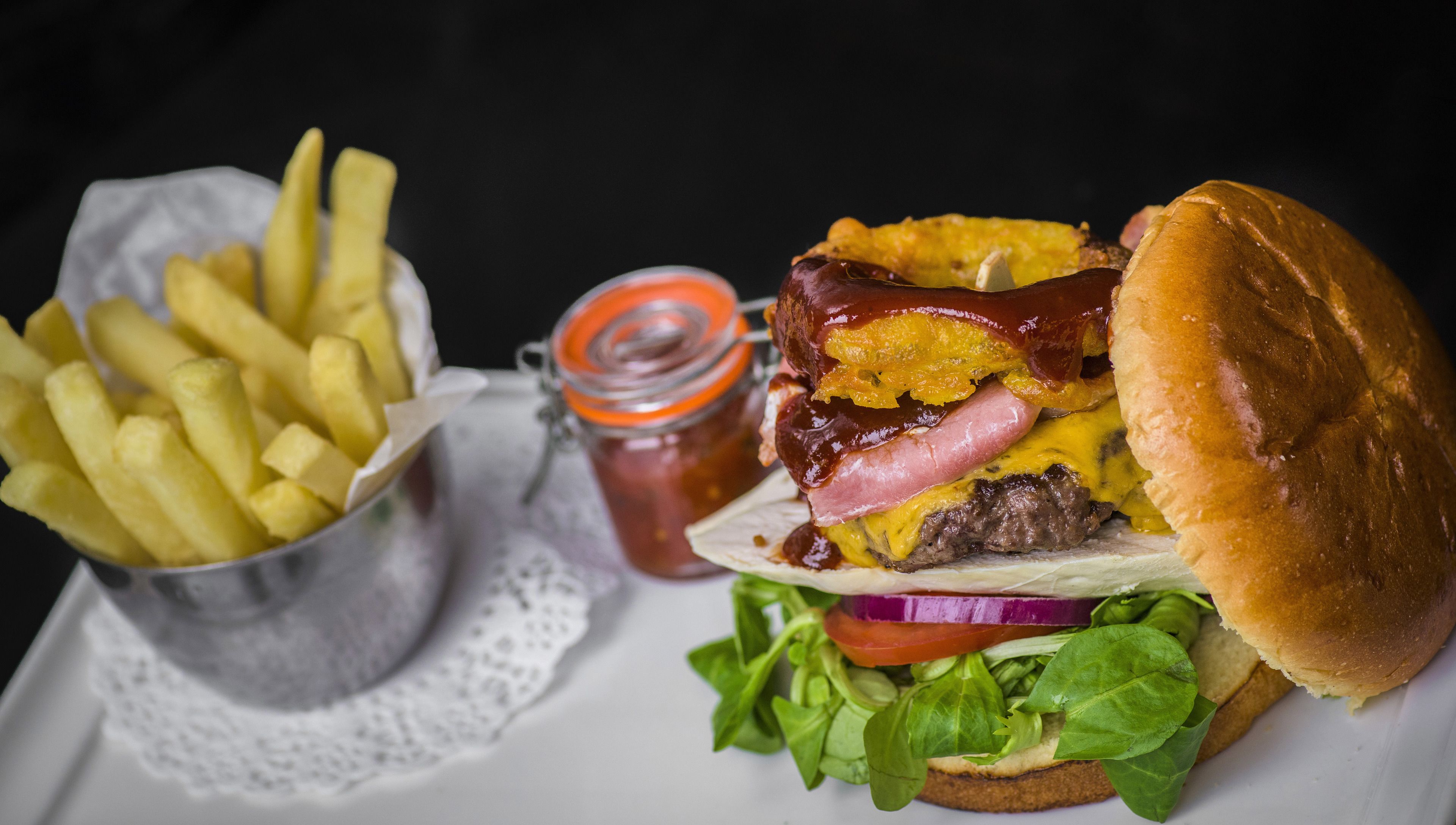 Un hamburger garni de laitue, de tomate et d’oignon rouge, accompagné de frites et d’un pot de ketchup.