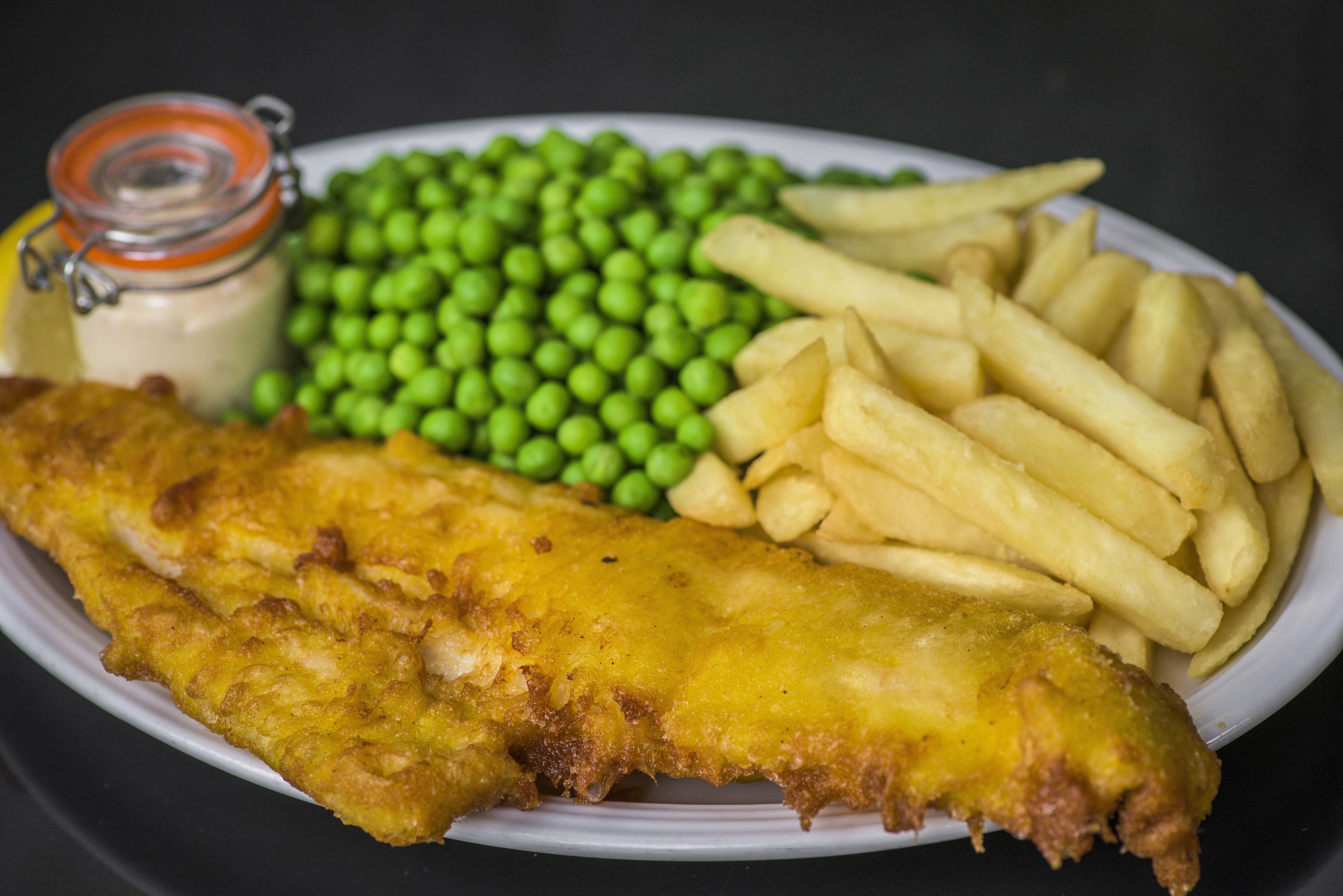 Um prato com peixe frito, batatas palha e um pequeno frasco de molho.