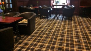 A room with a plaid carpet, leather chairs, a wooden table, and a lamp.