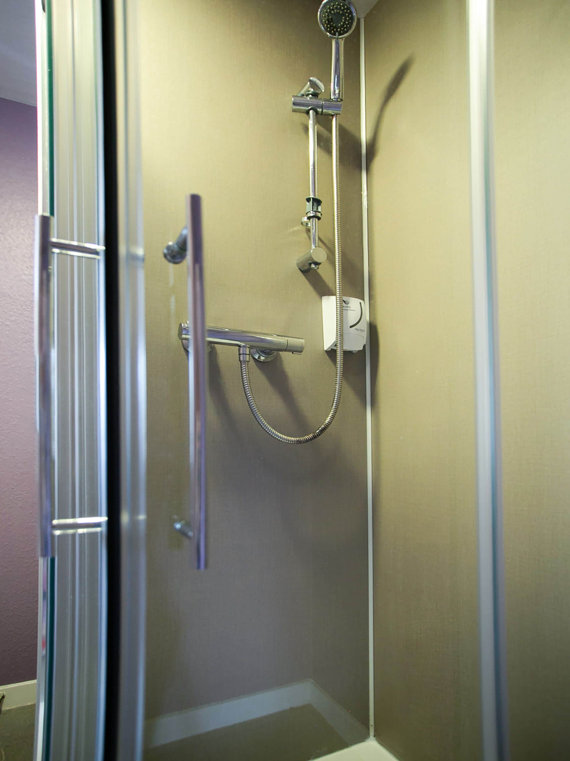 Een douche met een handdouche, een doucheaanslag en een kraan op de muur.