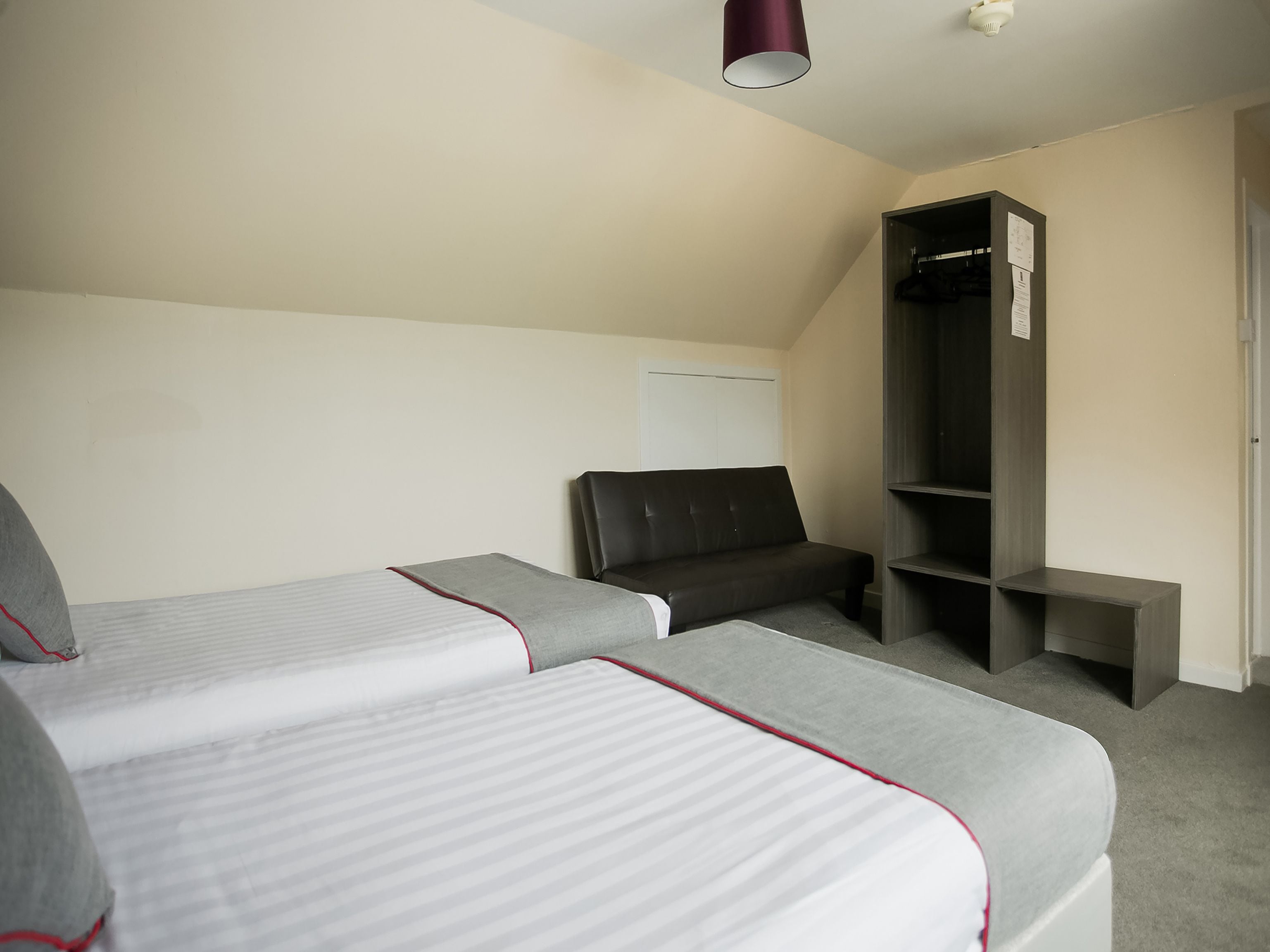 Ein Hotelzimmer mit zwei Einzelbetten, einem dunkelbraunen Ledersessel, einem kleinen Schreibtisch und einem Kleiderschrank.