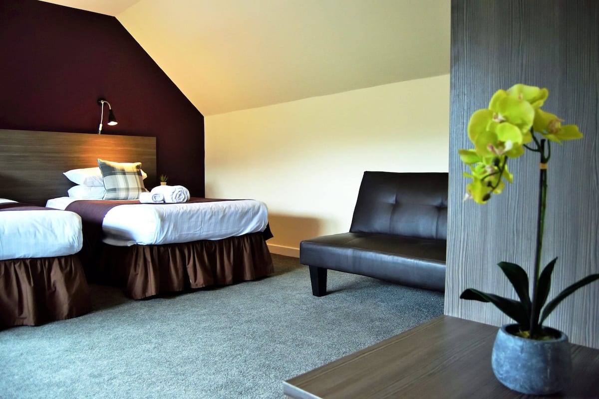 A hotel room with two beds, a sofa, a desk, and a potted orchid.