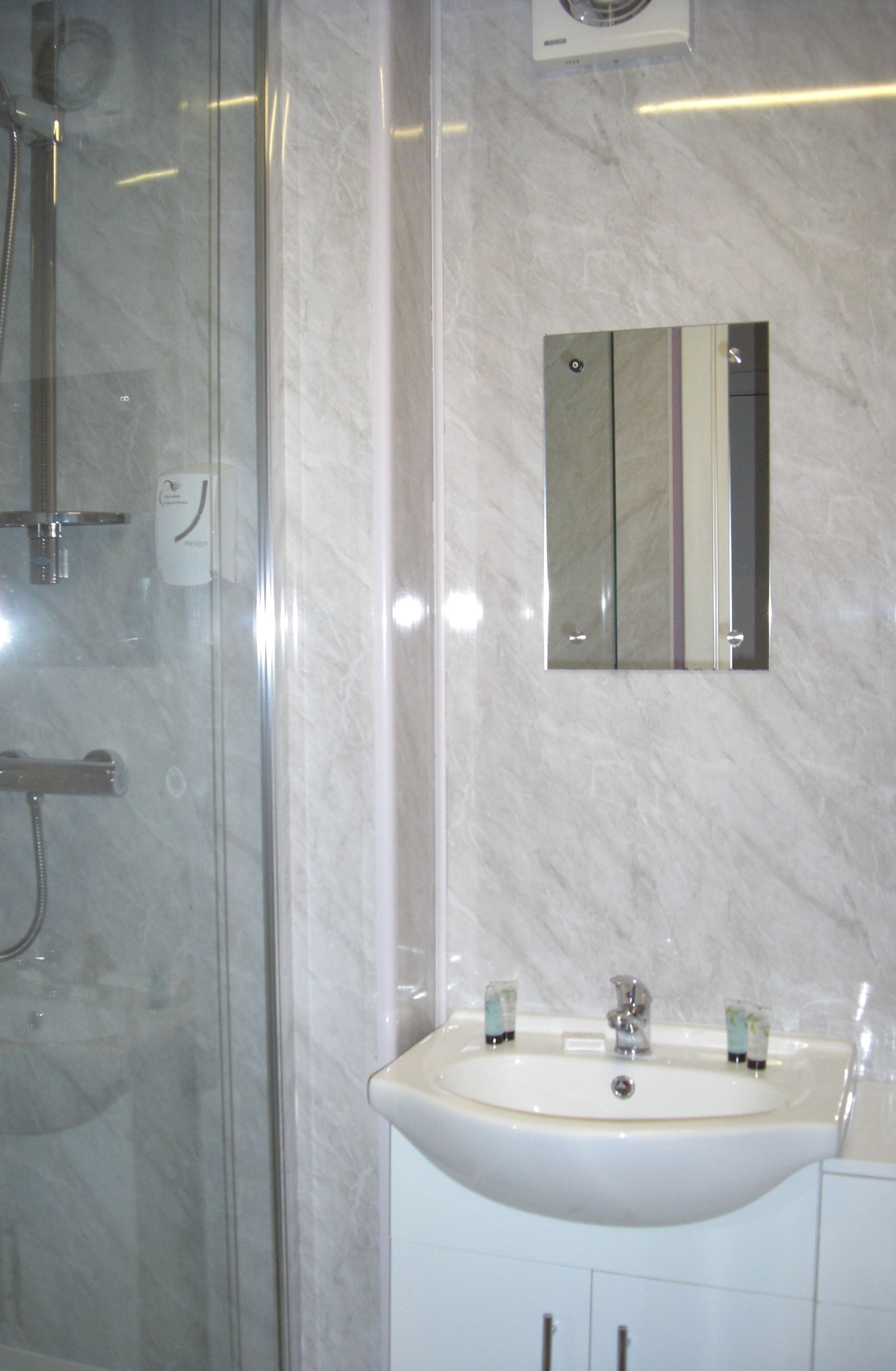 A bathroom with a glass shower enclosure, a sink with a mirror above it, and a marble wall.