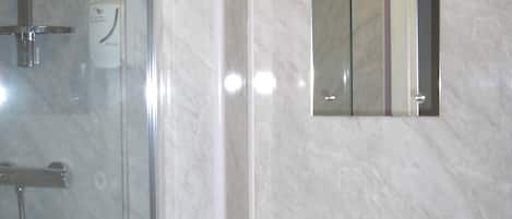 A bathroom with a glass shower enclosure, a sink with a mirror above it, and a marble wall.